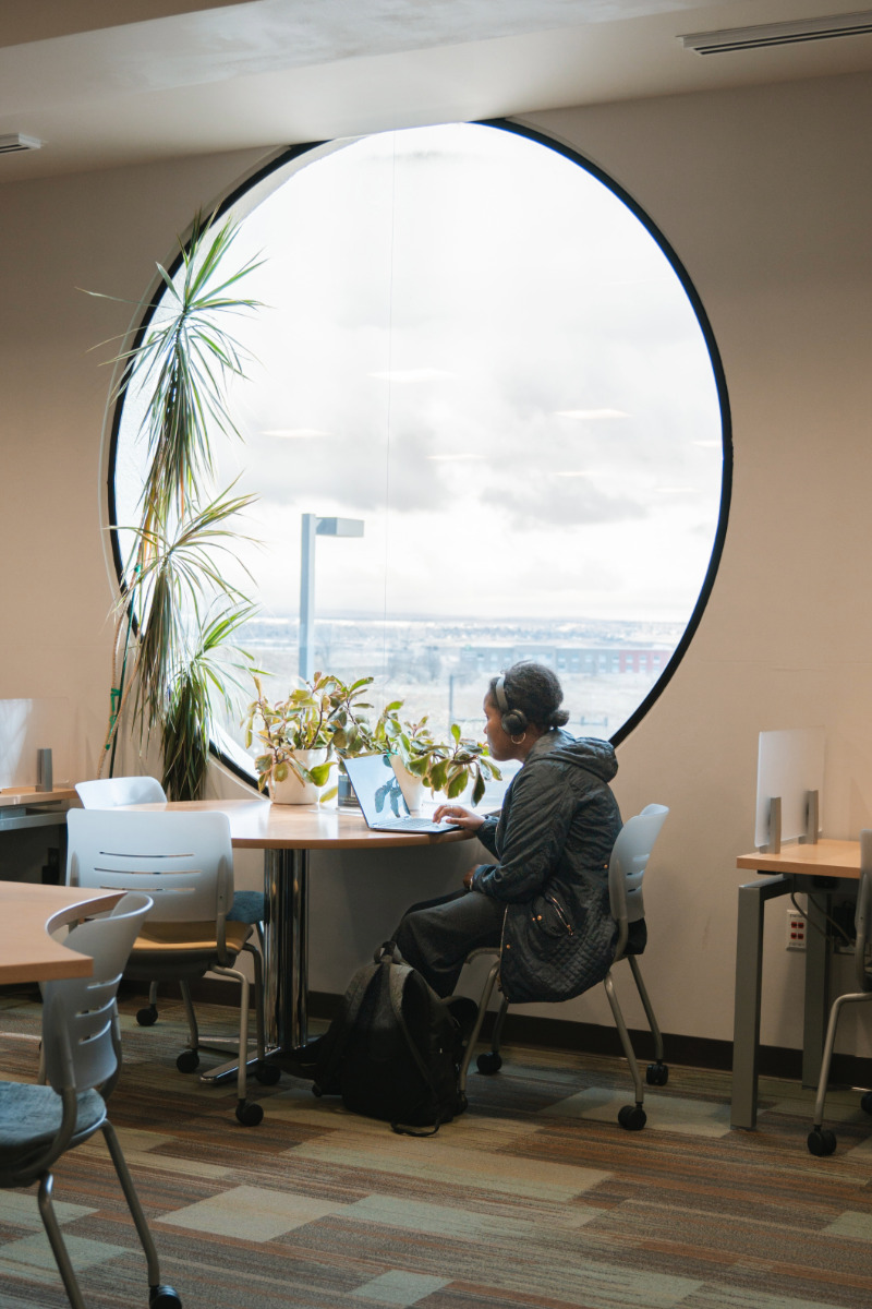 student working next to big round window in learning commons